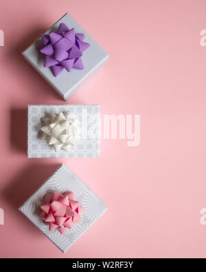 Three light gray gift boxes with colorful bows on pink background. Festive concept. Flat lay. Stock Photo