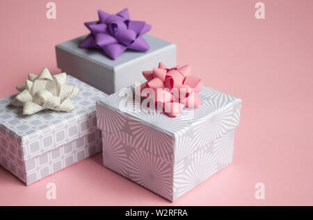 Three light gray gift boxes with colorful bows on pink background. Festive concept. Stock Photo