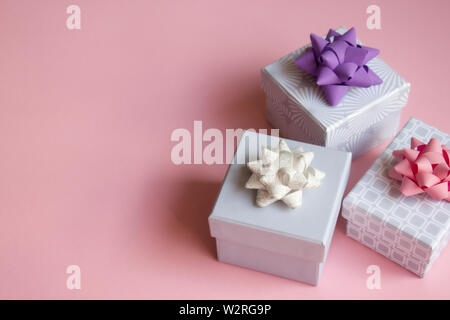Three light gray gift boxes with colorful bows on pink background. Festive concept. Flat lay. Stock Photo