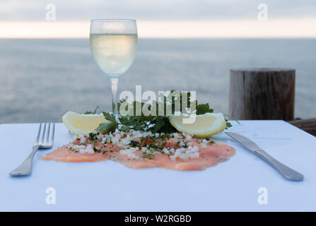 Delicious smoked salmon fillet with celery, onion, slices of ripe lemon and a glass of wine on a white table - The deep sea Stock Photo