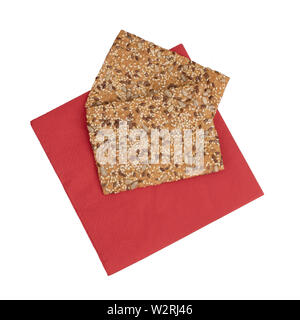 Healthy snack, wholemeal, wholewheat crackers with sunflower, linseed and sesame seeds. On red paper serviette, napkin, isolated on white background. Stock Photo