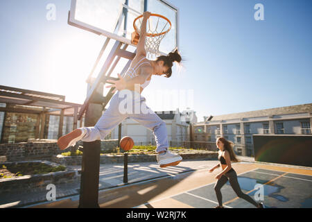 Two young women playing basketball on street court on a sunny day. Women playing a streetball game outdoors. Stock Photo