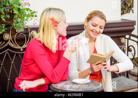 Female literature. Book every girl should read. Girls friends sitting cafe terrace drinking coffee. Reading inspiring book. Self improvement and education. Discussing popular bestseller book. Stock Photo