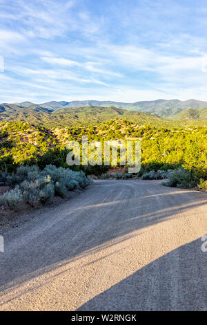 Sunset Santa Fe, New Mexico mountains vertical view in Tesuque with golden hour light on green plants and dirt road to residential community Stock Photo