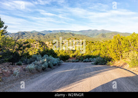Sunset Santa Fe, New Mexico mountains in Tesuque with golden hour light on green plants and dirt road to residential community Stock Photo