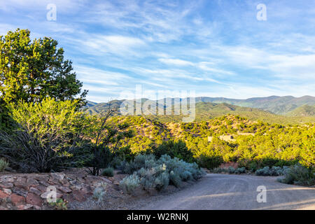 Sunset Santa Fe, New Mexico in Tesuque with golden hour light on green plants and dirt road to residential community Stock Photo