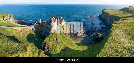 Ruins of medieval Dunluce Castle on a steep cliff. Northern coast of County Antrim, Northern Ireland, UK. Aerial wide panorama in sunrise light Stock Photo