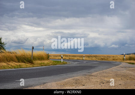 bend in a road with ripe wheat field in front of dramatic sky with storm clouds Stock Photo