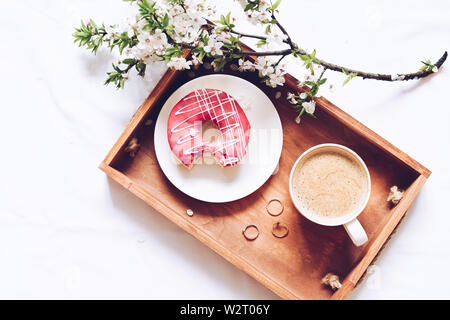 Spring brealfast in bed. Tray with strawberry pink donut with coffee and spring blossom. Romantic Valentine's day breakfast in bed for loved one. Moth Stock Photo