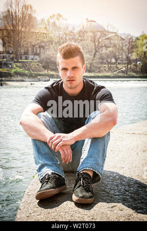 Contemplative young man sitting beside river in Turin Stock Photo