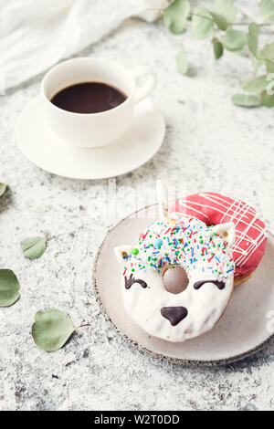 Cakes donuts with a cup of espresso over light background. Table with morning breakfast dessert and coffee. Trendy doughnut unicorn with white glaze. Stock Photo