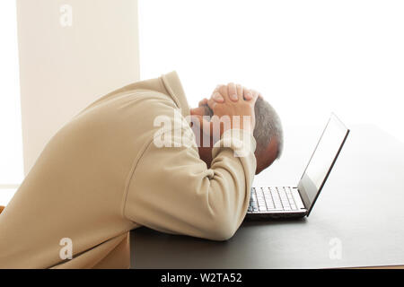 A man bends his head over computer in despair while he puts his hands over his head.  - Image Stock Photo