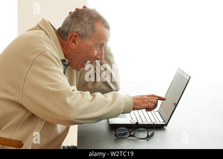 A man sits looking very surprised with open mouth as he points to the screen of a notebook computer. He reads or sees someting very surprising or funn Stock Photo