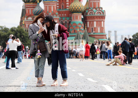 Asian girls tourists view photos on a smartphone standing on the Red square in Moscow on background of St. Basil's Cathedral. Happy young women Stock Photo