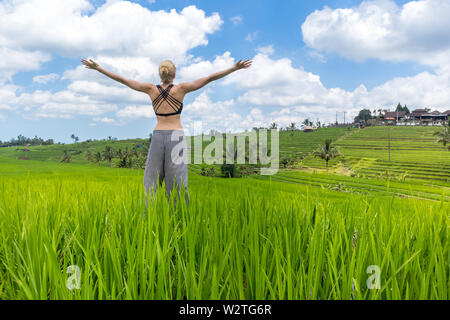 Relaxed healthy sporty woman, arms rised to the sky, enjoying pure nature at beautiful green rice fields on Bali. Stock Photo