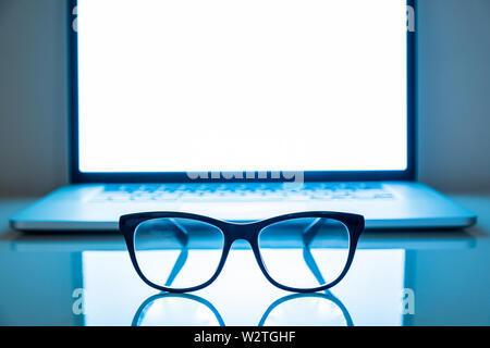 Computer eyeglasses in front of a laptop, low-key image. Blue light blockers and laptop in dark background, eye fatique problem concept Stock Photo