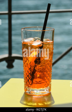 Close up view of a glass of Aperol Spritz on a table top with water in the background. No people. Stock Photo
