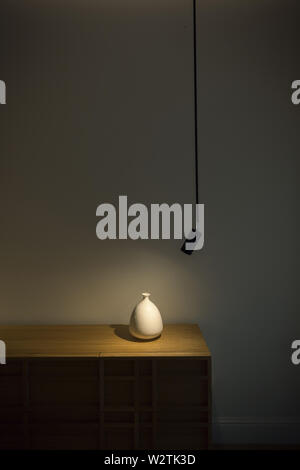 white vase on wooden shelf, spoted light, dark scene Stock Photo