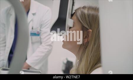 A beautiful girl is undergoing an ophthalmologic examination, checking her eye health and visual acuity. The laser beam shines into the patient's eye Stock Photo