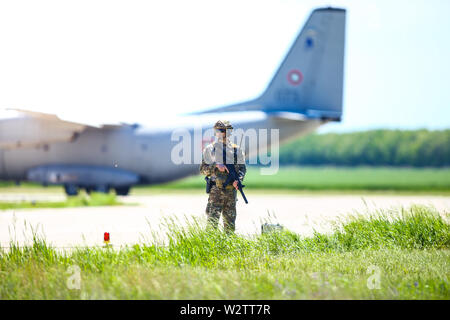 Boboc, Romania - May 22, 2019: Romanian army soldier patrols a military air base, with an Alenia C-27J Spartan military cargo plane from the Bulgarian Stock Photo
