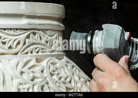 Closeup hands of unrecognizable craftsman using electric tool to polish floral ornament on plaster surface in workshop Stock Photo