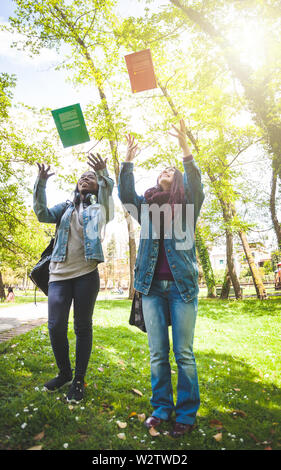 Two female students, one Caucasian and the other African, throw books into the air. End of studies concept. Stock Photo