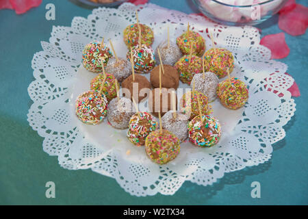 Balls of biscuit on a stick loli pop. cake pop. candy bar . Delicious and tasty dessert table with cupcakes . little coloured cakes on the plate for Stock Photo