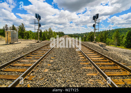 A long straight set of railroad train tracks disappear in the horizon through the mountains in the rural Inland Northwest area of North Idaho. Stock Photo