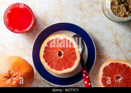 Grapefruit and fresh squeezed fruit juice, and brown sugar, healthy breakfast, on top of a light marble tabletop Stock Photo