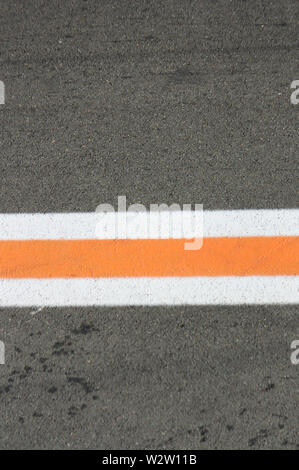 Asphalt colored background with a three horizontal stripes of white, orange and white horizontal that crosses the image in half Stock Photo