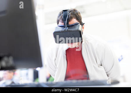 Young man wearing virtual reality headset and gesturing while sitting at his desk in creative office Stock Photo