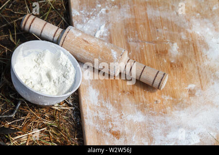 Top view of the working board with flour and rolling pin next to a bowl of flour that lies on the grass, the concept of cooking in nature and picnic Stock Photo