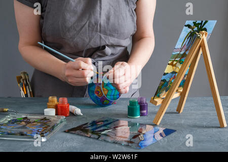 Painter holding a paintbrush in his hand and painting with stained glass paints on a glass vase. Stock Photo