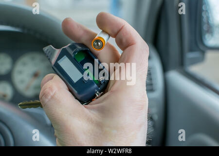 the hand of the person who is in the car holds the disassembled alarm keychain and a new battery for replacement Stock Photo