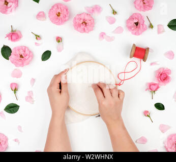 two female hands holding a round wooden hoop and a red thread with a needle, concept of embroidery products, top view Stock Photo