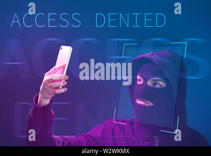 Female hacker in mask holding smartphone protected with facial recognition system Stock Photo