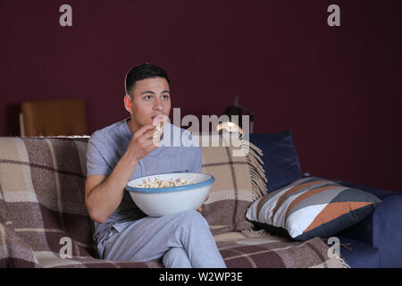 Handsome young man eating unhealthy food while watching TV at night Stock Photo