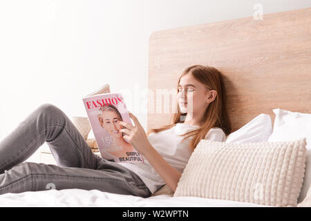 Cute teenage girl reading fashion magazine in bedroom at home Stock Photo