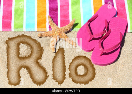 Rio. Overhead view ot the word RIO written on beach sand with a colorful striped towel, pink thongs and a starfish conceptual of a summer vacation and travel in Rio de Janiero, Brazil Stock Photo