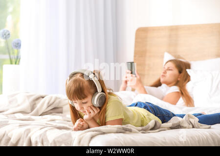 Little girl with addiction to modern technologies lying with mobile phone on bed at home Stock Photo