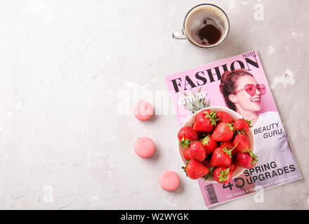 Bowl with ripe strawberry, fashion magazine, cup of coffee and macarons on light background Stock Photo