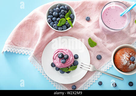 Tasty blueberry desserts with yogurt on color background Stock Photo