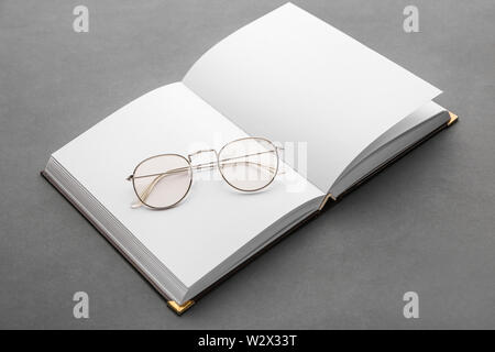 Open book with eyeglasses on grey background Stock Photo
