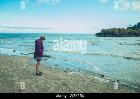 A senior woman is standing by the water's edge on the beach Stock Photo