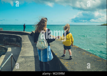 A young mother and her toddler are wealking on a pier by the sea in summer Stock Photo