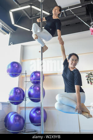 (190711) -- JILIN, July 11, 2019 (Xinhua) -- Jiang Zhijun (top) and Li Fengmei practice pole dancing in the dance room in Jilin City, northeast China's Jilin Province, July 10, 2019. A group of dama, refering to the legions of usually middle aged women, formed a team of pole dancing in Jinlin City, northeast China's Jilin Province in 2016. The team has eight members with an average age of 64. 'Pole dancing is known for its softness and strength,'says Jiang Zhijun, the 68-year-old team leader.' We started with basic strength training, then went forward to perform high-level moves gradually.' Th Stock Photo