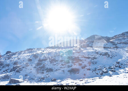 Sun on top of snow cover himalaya range. Frozen Rocky peak filled with deep snow illuminate rising sunlight in frosty winter day time. Blue clear sky. Stock Photo