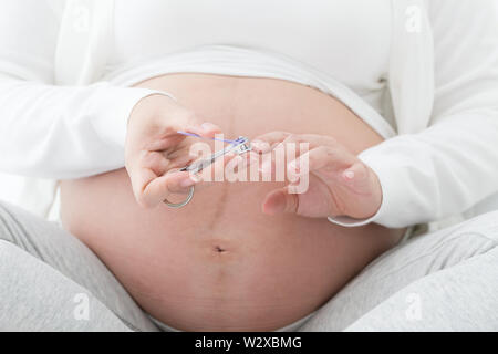 Pregnant woman cutting nails hand by nail clipper on white bed in the bedroom, Beauty treatments for nail care and manicure during pregnancy healthy c Stock Photo