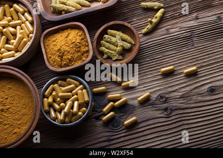 Curcuma capsules, turmeric roots and powder in bowls. Anti cancer medicine. Wooden table. Top view shot. Stock Photo