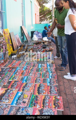 female Asian tourist browsing traditional African curios or souvenirs to buy from a black African street vendor in Bo Kaap, Cape Town, South Africa Stock Photo